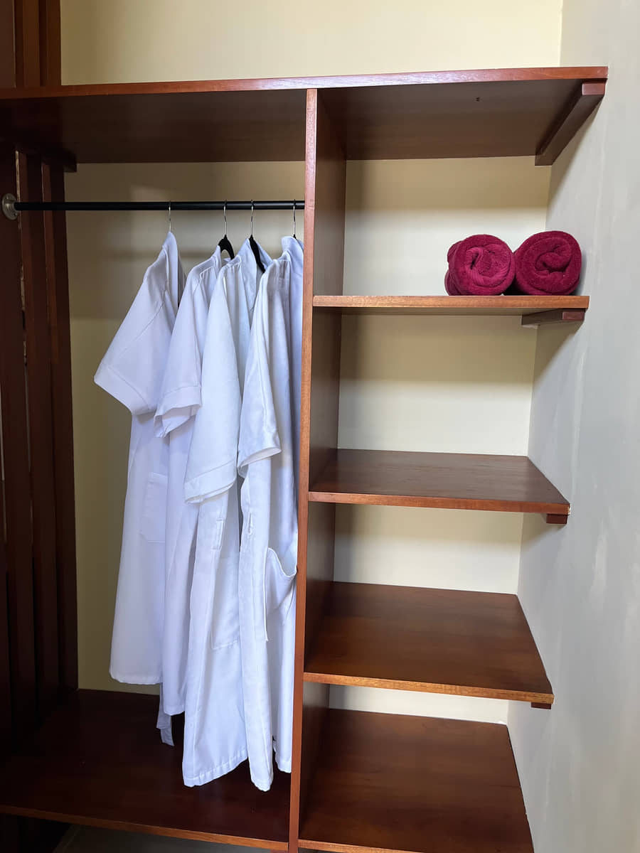 Las batas blancas de Reborn Spa colgadas en el armario de madera junto a las toallas enrolladas