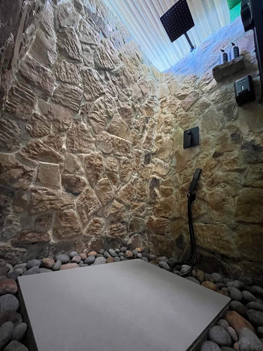La ducha abierta de piedra de Reborn Spa: muro de laja, piso de canto rodado y regadera tipo lluvia