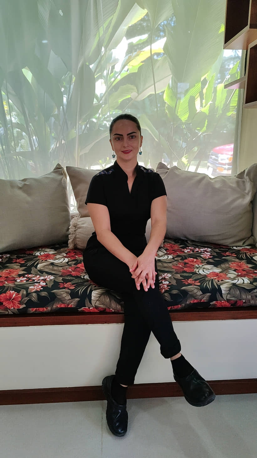 Terapeuta de Reborn Spa sentada en el diván de la ventana, uniforme negro, con el jardín detrás