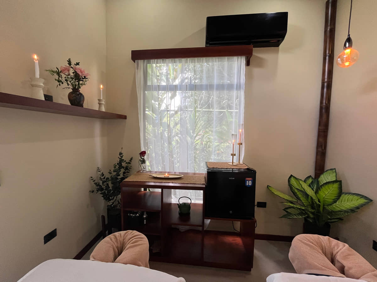 Rincón de la sala de Reborn Spa: velas encendidas, flores y cortina de lino con el jardín detrás